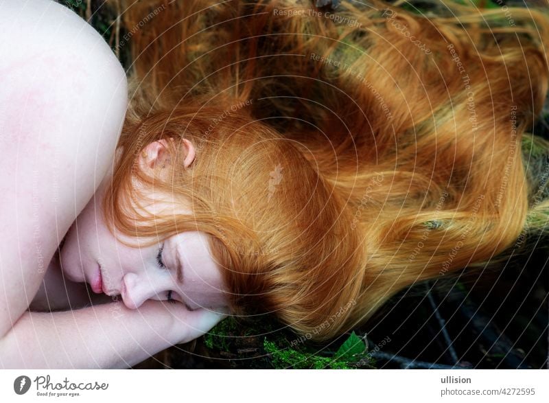 Portrait of a nude young charming sexy woman redhead lying in the autumn forest, her long red hair placed around her head. ground woods pretty attractive fairy