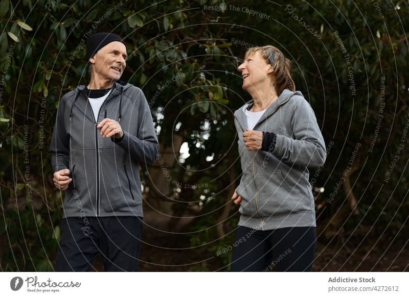 Positive elderly couple running together in park senior training fitness cardio activity active positive man woman wellbeing healthy sport sportswear wellness