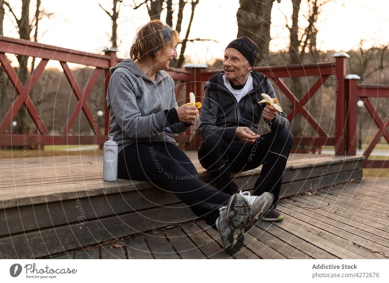 Positive aged couple eating bananas after workout senior rest talk break wellness food positive man woman together elderly retire old pensioner fruit tasty