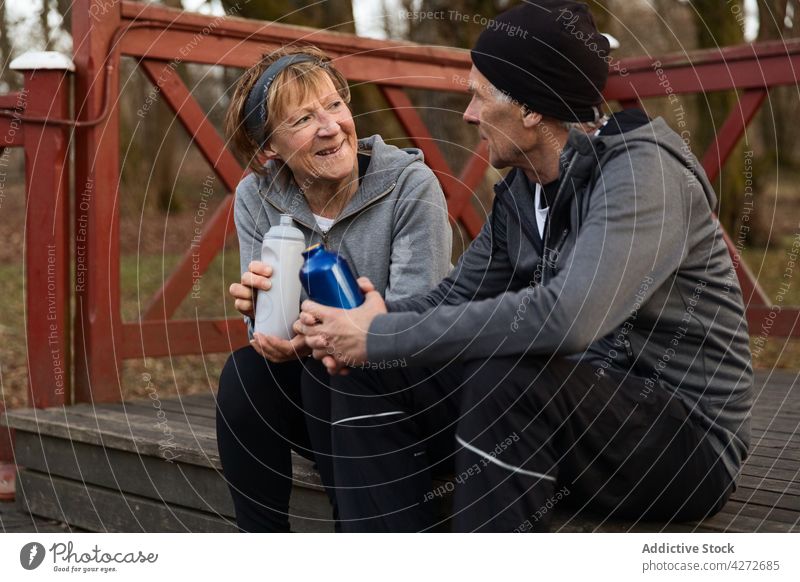 Positive aged couple talking to each other after workout break training bottle speak recreation refreshment together positive man woman senior retire pensioner
