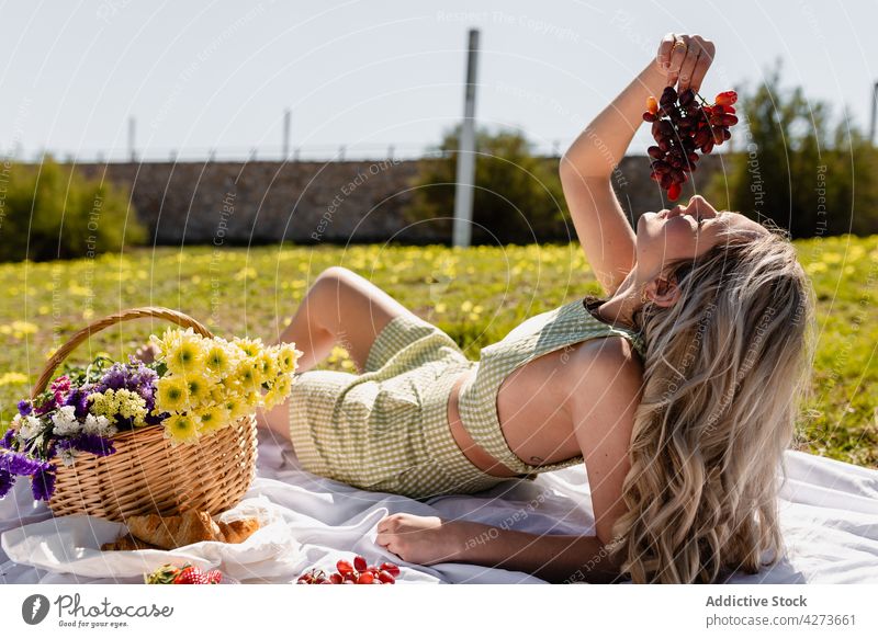 Young woman eating bunch of grapes on picnic fruit basket flower nature countryside glade female food fresh bloom tasty ripe blossom plant rural vitamin lying