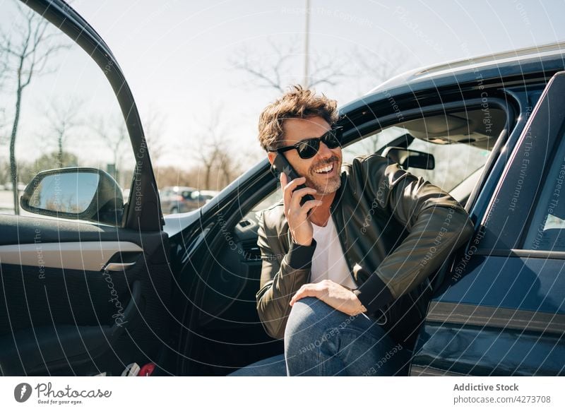 Cheerful man talking on smartphone in car speak message happy town using gadget device masculine cellphone conversation content smile glad enjoy free time sit