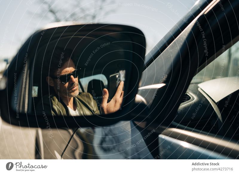 Driver reflecting in side mirror while browsing smartphone driver watching reflection car masculine sunglasses man using gadget serious device phone call brutal