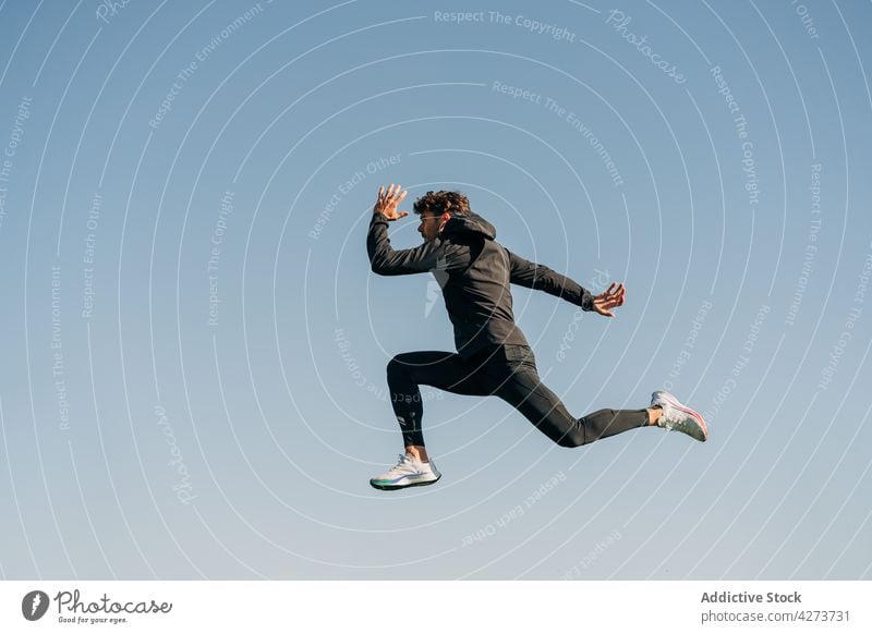 Fast runner jumping during workout under blue sky sport energy speed fast dynamic man training sportsman masculine rapid motion leap athlete fit wellbeing