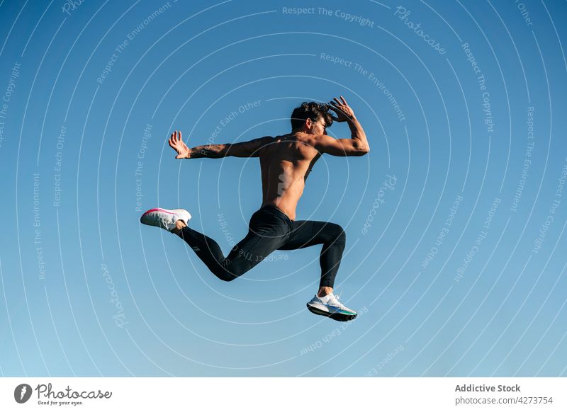 Fast runner jumping during workout under blue sky sport energy speed fast dynamic shirtless naked torso man training sportsman masculine rapid motion leap