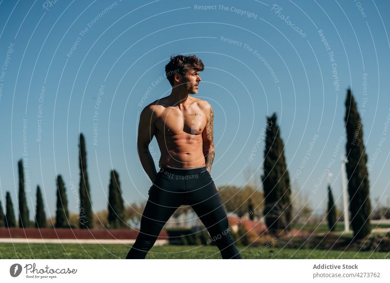 Muscular sportsman performing side bend during training in park athlete wide legs workout abdomen exercise abs shirtless naked torso stand practice masculine