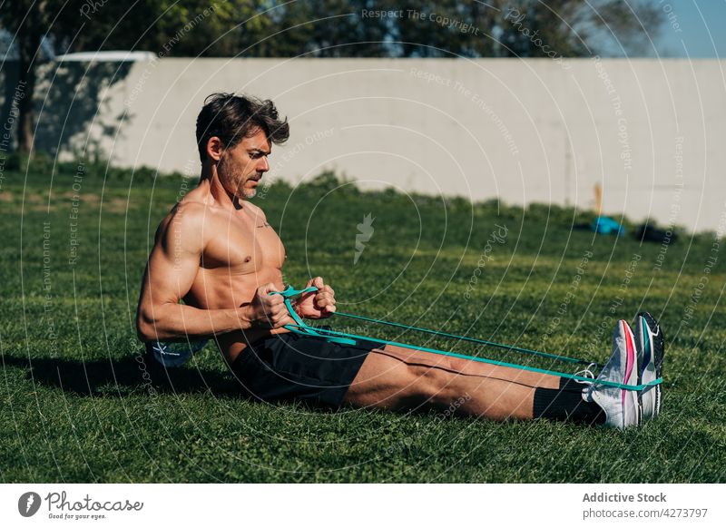 Strong sportsman exercising with resistance band on lawn exercise training workout stretch muscular strong bicep practice activity elastic band shirtless