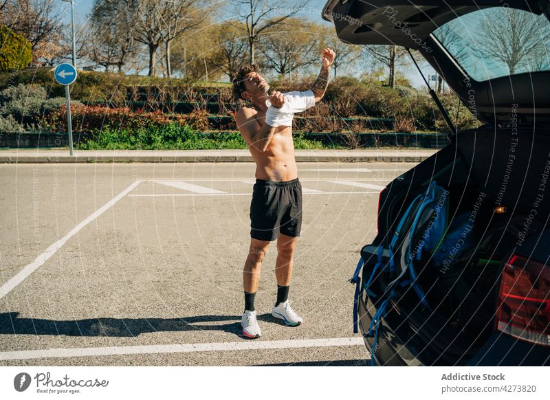 Muscular sportsman putting on t shirt against car put on abdomen sporty masculine macho parking pavement city town automobile belly tattoo body curve muscular