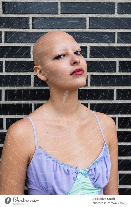 Serious hairless female standing near brick wall woman bald serious alone makeup street confident individuality town young daylight feminine city pensive