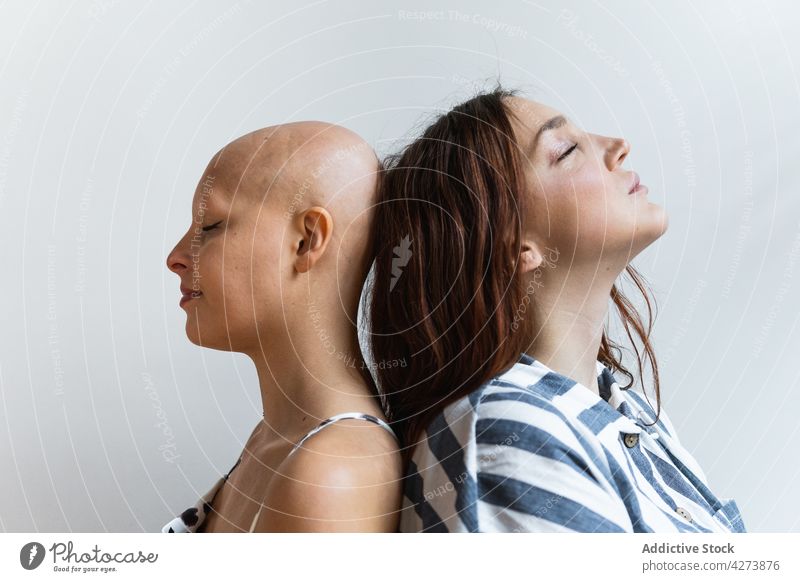 Young female friends standing back to back with closed eyes women eyes closed best friend alopecia problem support together personality relationship feminine