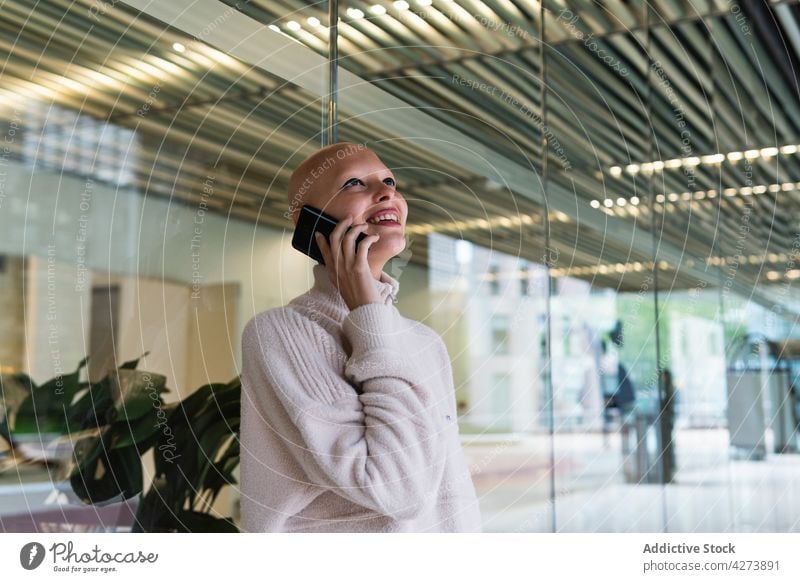 Smiling young bald lady talking on smartphone in office woman smile phone call alopecia conversation communicate discuss positive work female sweater style
