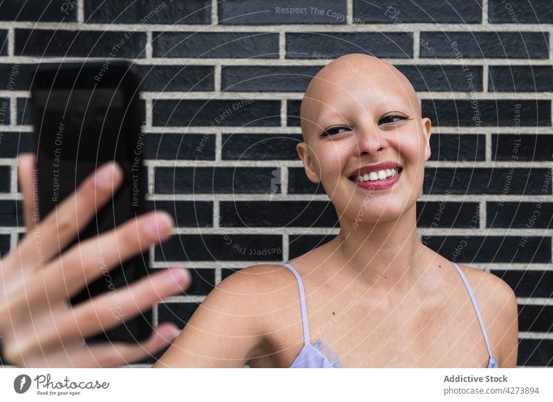 Smiling bald woman taking selfie on phone near brick wall smartphone smile street modern happy female young device mobile gadget using lifestyle city urban