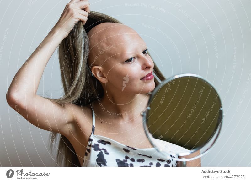 Young woman taking off wig and looking in mirror confident take off alopecia disease appearance personality feminine individuality makeup female young long hair
