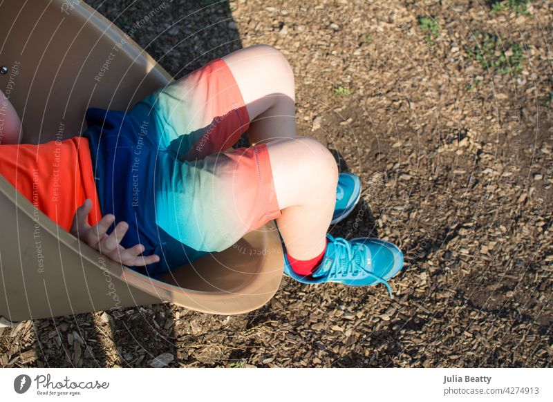 At the end of slide: boy exits a tube slide wearing colorful clothes and shoes rainbow playground climb park equipment recess Vestibular athletic shorts