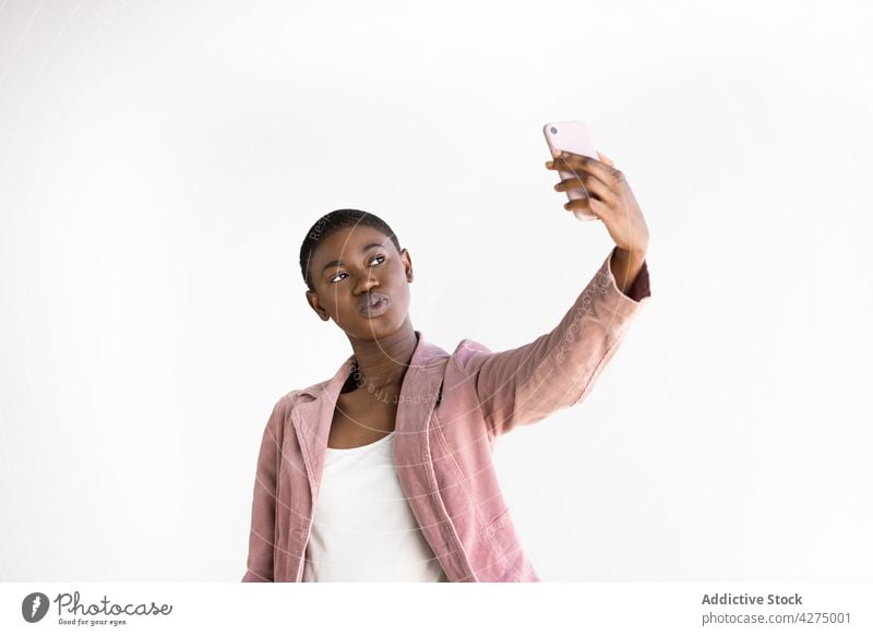 Stylish black woman taking selfie on smartphone fashion kiss style happy moment memory enjoy using gadget device self portrait cellphone satisfied jacket trendy