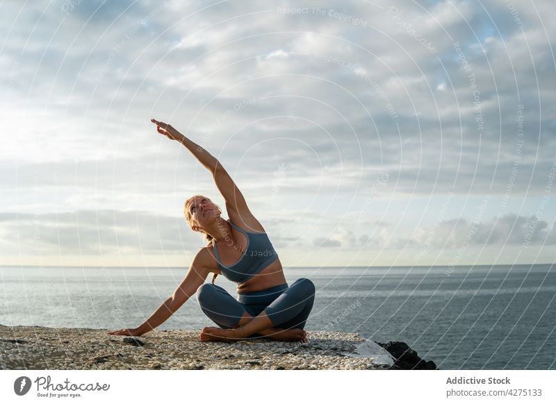 Woman practicing yoga with raised arm on sea shore woman practice legs crossed arm raised side bend vitality wellness ocean coast evening healthy lifestyle