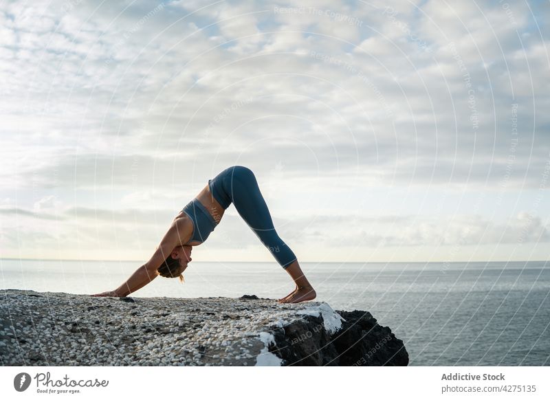 Flexible woman showing Downward Facing Dog pose against ocean yoga downward facing dog stretch flexible forward bend healthy lifestyle vitality sea sky cloudy