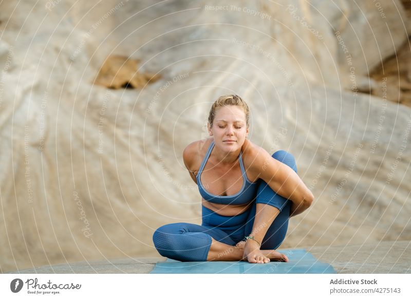 Woman showing Sage Marichis pose against mountain woman yoga stretch sage marichis eyes closed hand behind back lean forward concentrate wellness practice