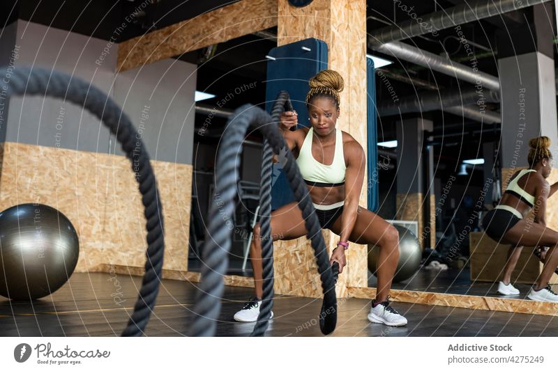 Determined black sportswoman working out with heavy ropes in gymnasium battle training functional fitness motivation strength cardio power workout exercise