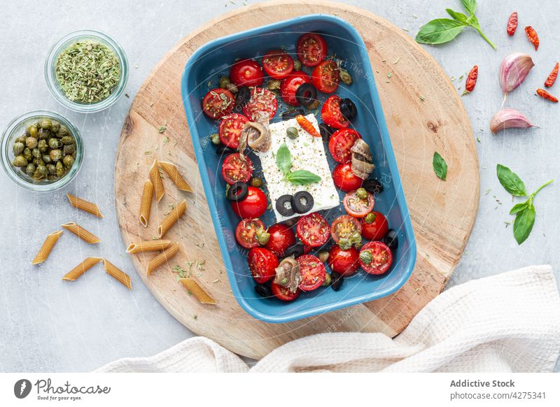 Baked cherry tomato halves with feta cheese in baking pan olive anchovy culinary recipe penne pasta baked food uncooked spoon baking dish tasty puttanesca half