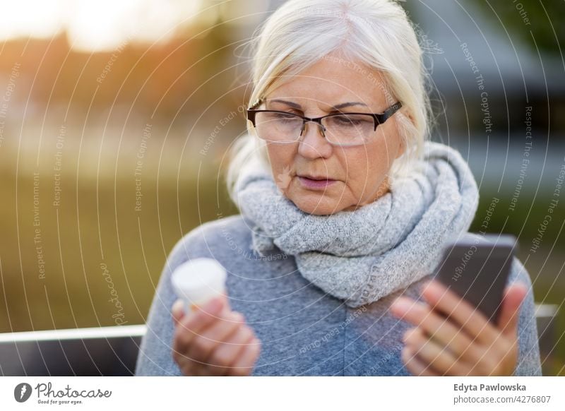 Woman holding smartphone and pill bottle senior seniors pensioner pensioners woman casual outdoors one person retiree retired outside retirement aged female