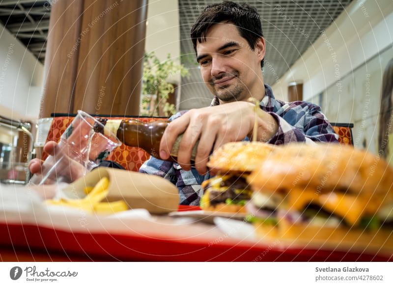 man eating fast food burger and drinking beer alone in the open area of a restaurant in a shopping mall meal bar happy pub male people lunch dinner hamburger