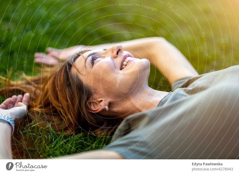Carefree woman lying on the grass in the sun high angle daydreaming above rest green lawn meadow park nature spring red hair redhead sunny outside pretty girl