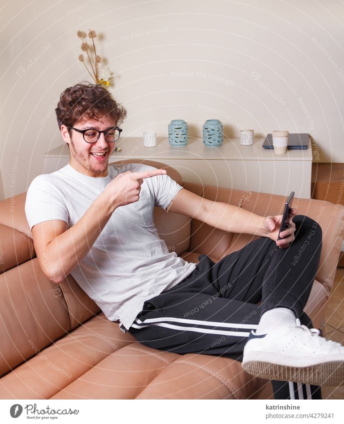 Young men making video call with phone  while sitting on the sofa at home point mockup t-shirt videocall smart phone cell phone mobile phone Lifestyle jeans