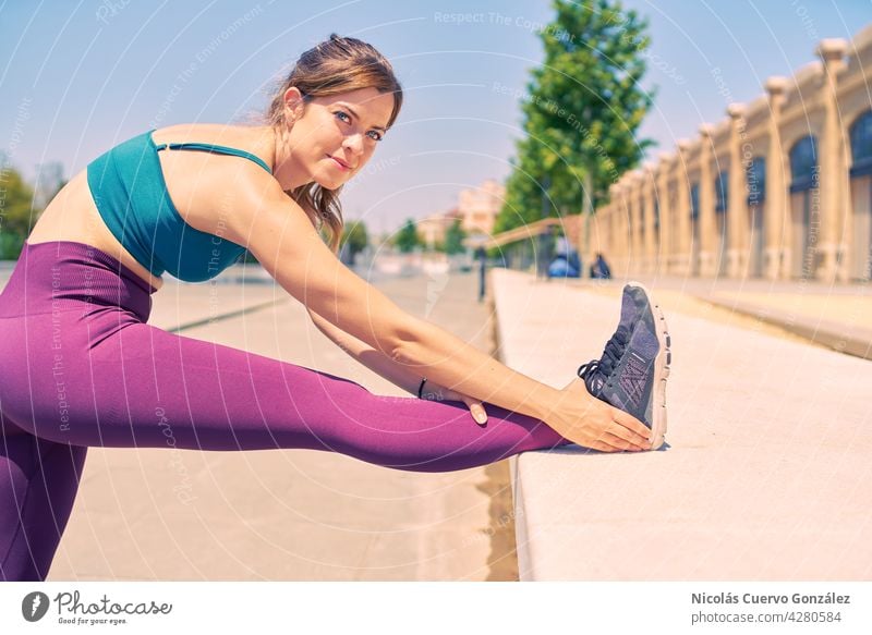 Attractive woman with beautiful blue eyes stretching her leg while looking happy during a summer morning in a city park. fitness outside health sport attractive