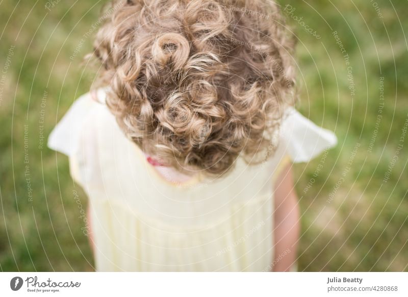 Young girl with short blonde curly hair wearing a vintage yellow flower girl dress; view of top of head and hair coil wavy natural child kid retro heirloom bob