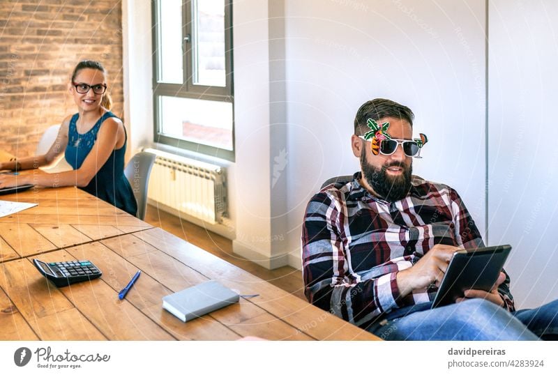 Businesswoman looking at her colleague who is wearing funny glasses because he is going on vacation office worker summer sunglasses last day smiling working