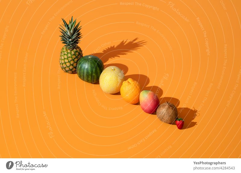 Summer fruits in bright light aligned on an orange background. above ananas arranged cantaloupe citrus coconut color copy space creative cut out delicious diet
