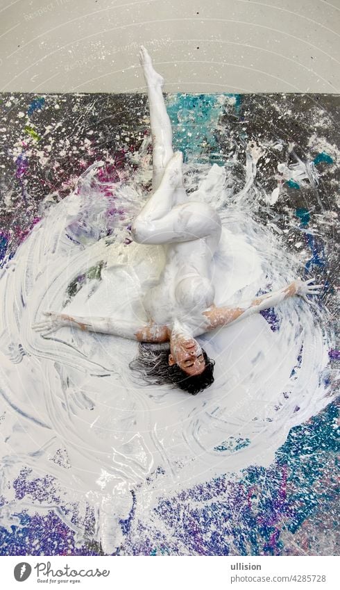 Young sexy dark haired woman, artistically abstract painted with white paint, lies on the two-colored studio floor, copy space body young bodypainting body art
