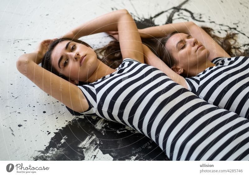 two sexy young women sisters girlfriends in black and white striped dress lying on the painted artists floor friendship camaraderie brunette woman lady elegance