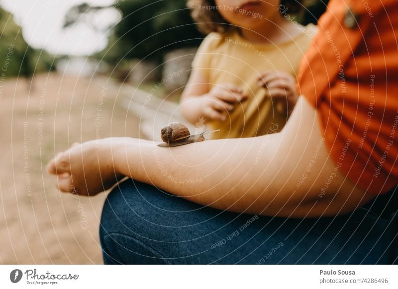 Child looking at snail crawling on mother's arm Snail Snail shell Mother childhood Parenting Exterior shot Animal Nature Colour photo Day 1 Close-up Crawl