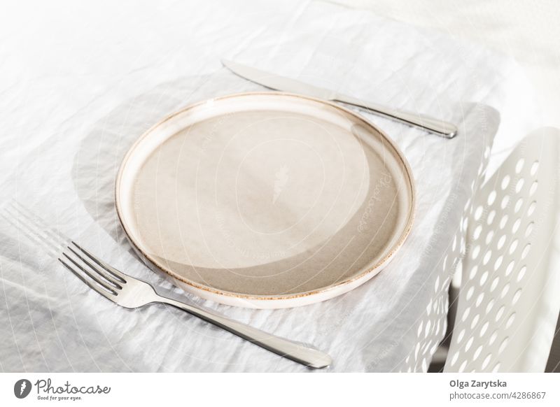 Empty plate on white linen tablecloth. empty setting sunlight nobody angle view minimal one chair wall kitchen