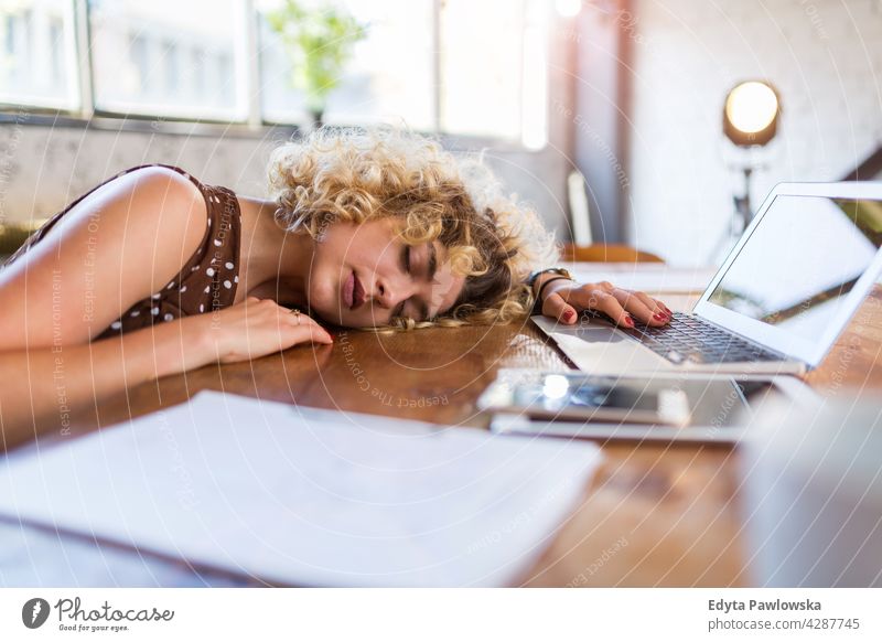 Young businesswoman asleep at her desk in an office businesspeople businessperson caucasian female indoors informal casual young adult students employee success