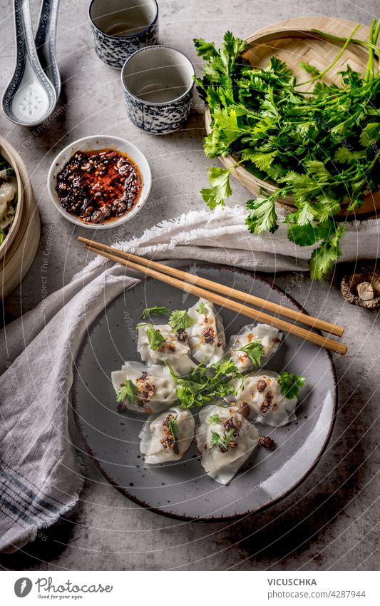 Asian dumplings served with traditional crockery, chopsticks, bundle coriander and chili sauce. Grey concrete background. Top view copy space asian dumplings