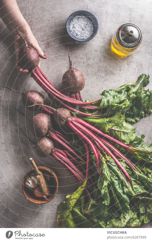 Women hand holding beet bunch with greens and healthy ingredients for cooking. Top view freshness rustic copy space woman hands beetroot surrounded oil dark