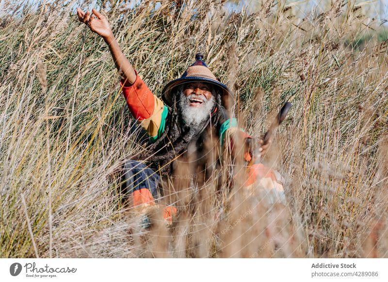 Happy hippie rastaman standing on field rastafarian happy smile male delight cheerful culture ethnic reggae caribbean nature african american native meadow hat
