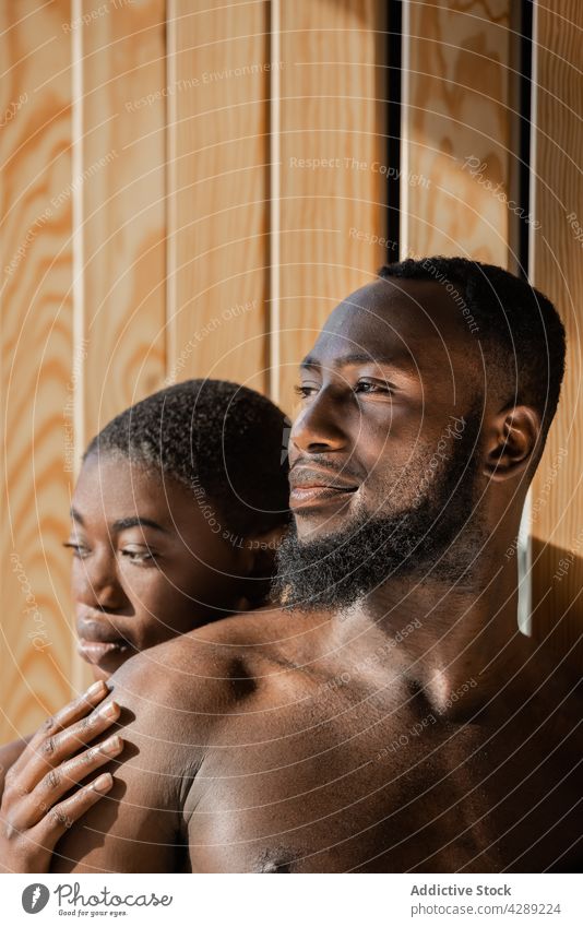 Romantic black couple leaning on wall in sunlight romantic love together relax bare shoulders shirtless relationship confident portrait serious pensive calm