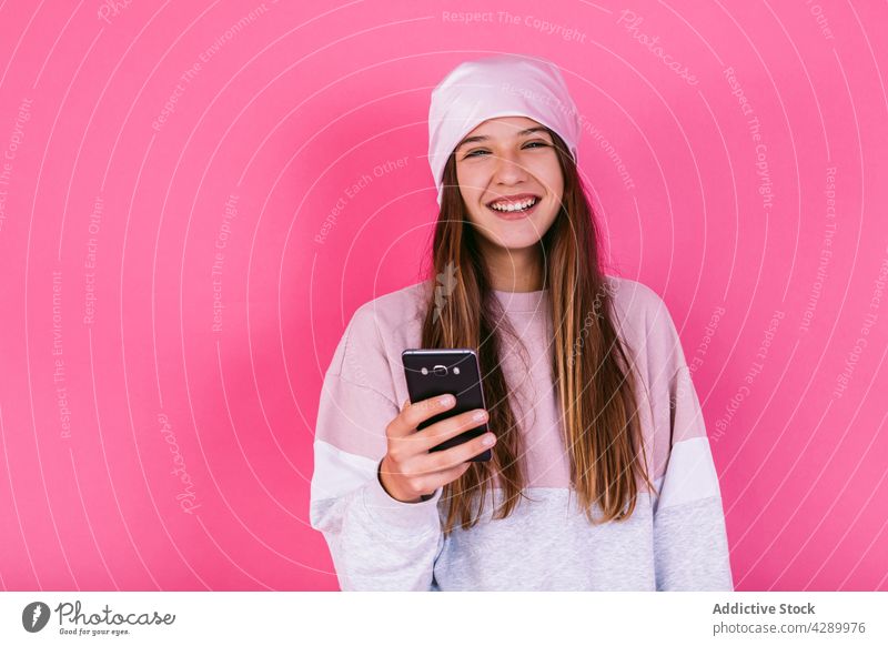 Happy teen on smartphone on pink background adolescent cancer happy browsing headscarf woman oncology millennial portrait chemotherapy using sick gadget device