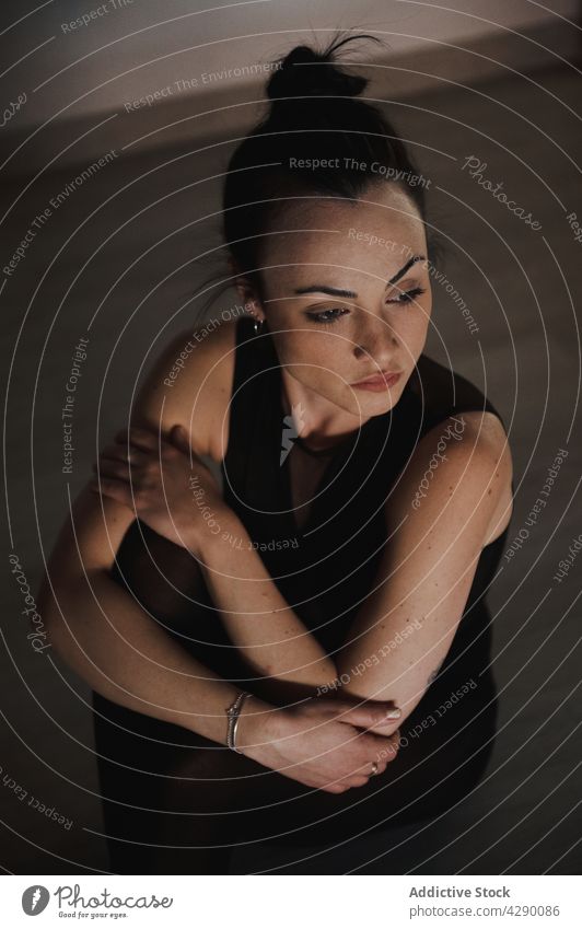 Gentle woman in sportswear resting on parquet charming sincere gentle tender alone portrait sit black color lonely shade solitude wall floor harmony feminine