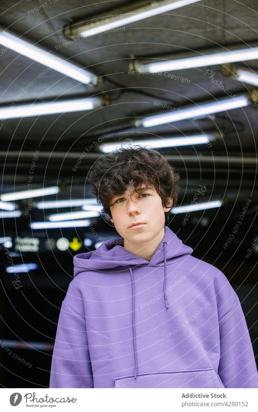 Stylish teenager standing under illuminated ceiling boy adolescent street style urban glow lamp roof casual hoodie light serious trendy appearance bright gaze