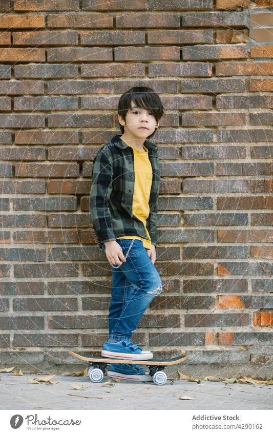 Little boy standing with skateboard on brick wall background kid street childhood hobby ethnic sporty skateboarder street style carefree casual trendy cute