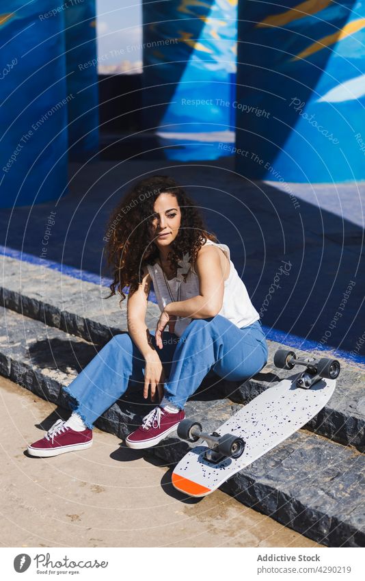 Pensive woman sitting on steps with skateboard hobby sporty street stair city street style thoughtful skateboarder urban female positive curly hair pensive