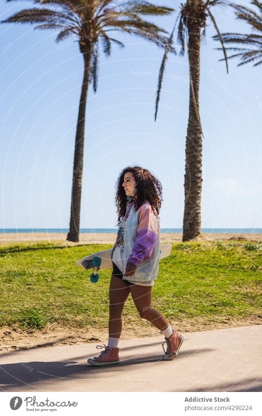 Woman with skateboard walking near embankment woman skateboarder hobby beach coast sport seafront sidewalk longboard female casual sporty young exercise