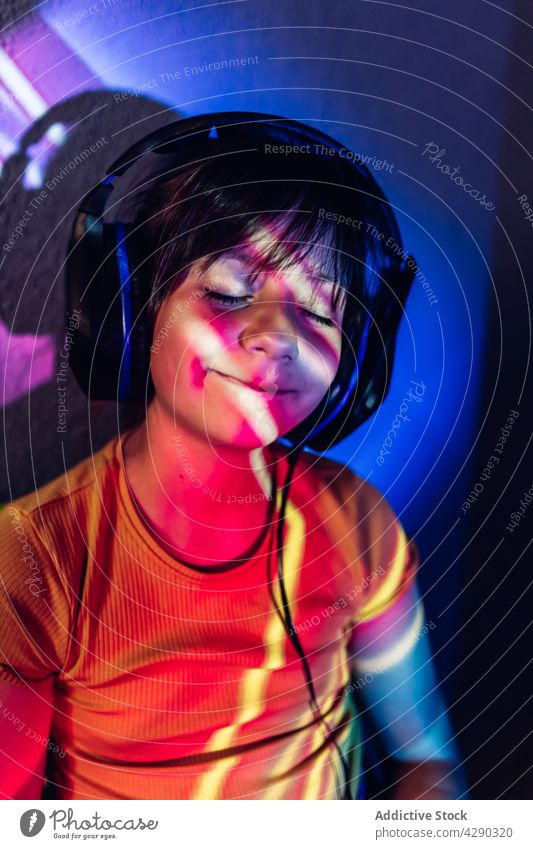 Content girl using tablet and listening to music in headphones browsing gadget cheerful content eyes closed neon light kid casual surfing connection enjoy