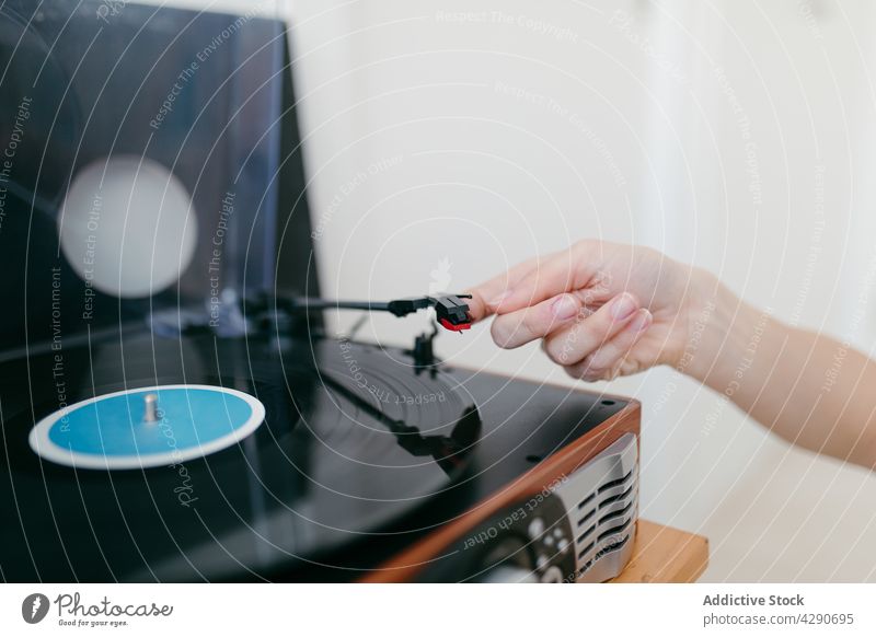Unrecognizable woman turning on turntable with vinyl record at home turn on player nostalgia retro music using device song melody audio spare time sound vintage
