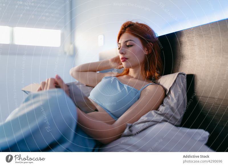 Woman reading book while resting on bed at home woman literature free time interested gentle spare time shiny soft pillow lying attentive relax pastime idyllic